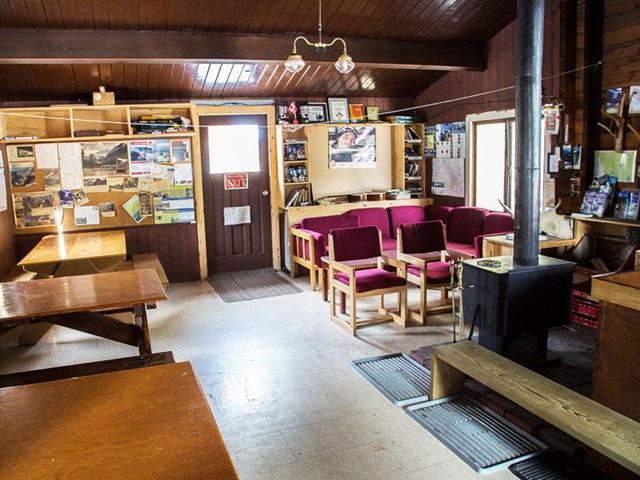 Rustic lounge with wood stove, red chairs, skylights, and photo-filled bulletin boards.