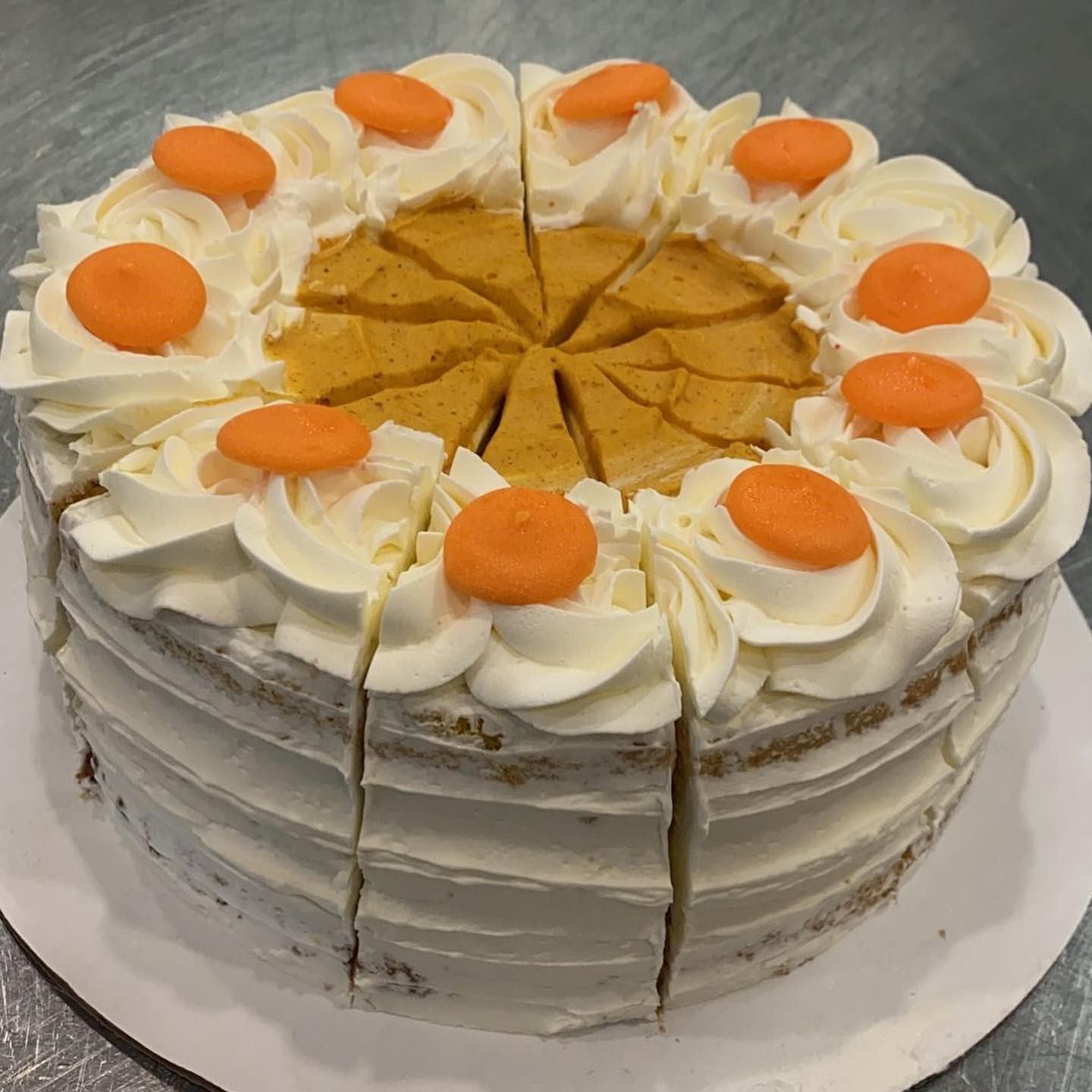 Frosted cake sliced into 12 pieces, topped with orange decorations and white dollops.