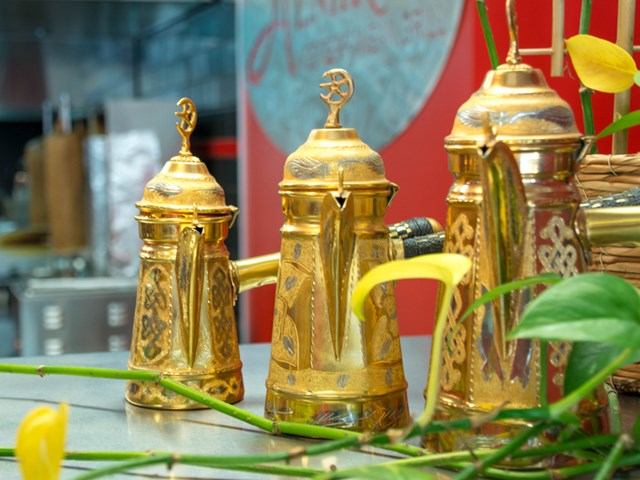 Ornate golden coffee pots with floral decor, set against a red background.