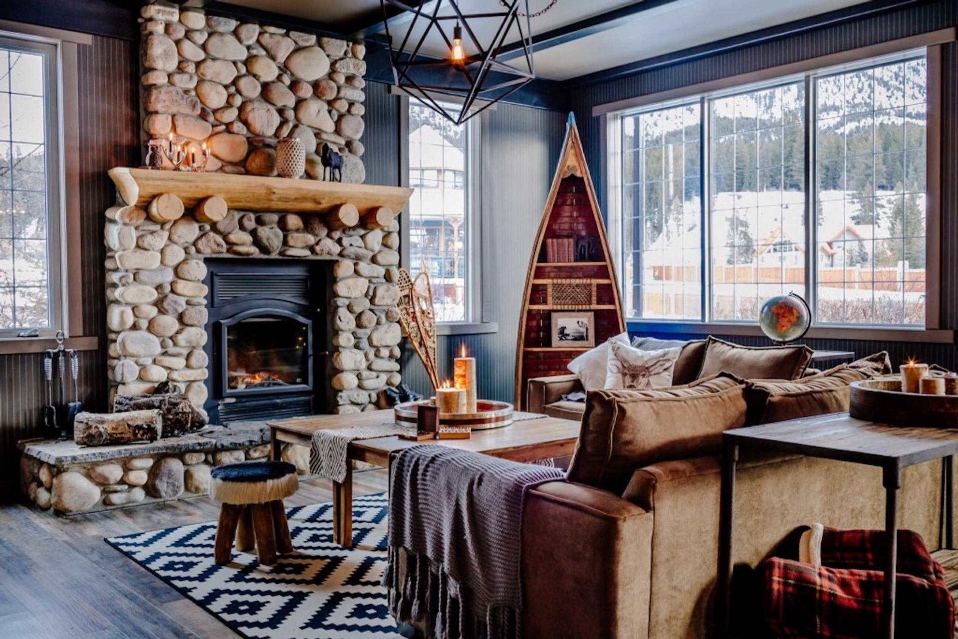 Rustic seating area with stone fireplace, wood décor, and large windows facing mountains.
