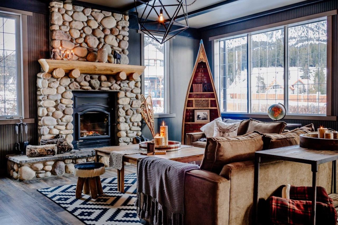 Rustic seating area with stone fireplace, wood décor, and large windows facing mountains.