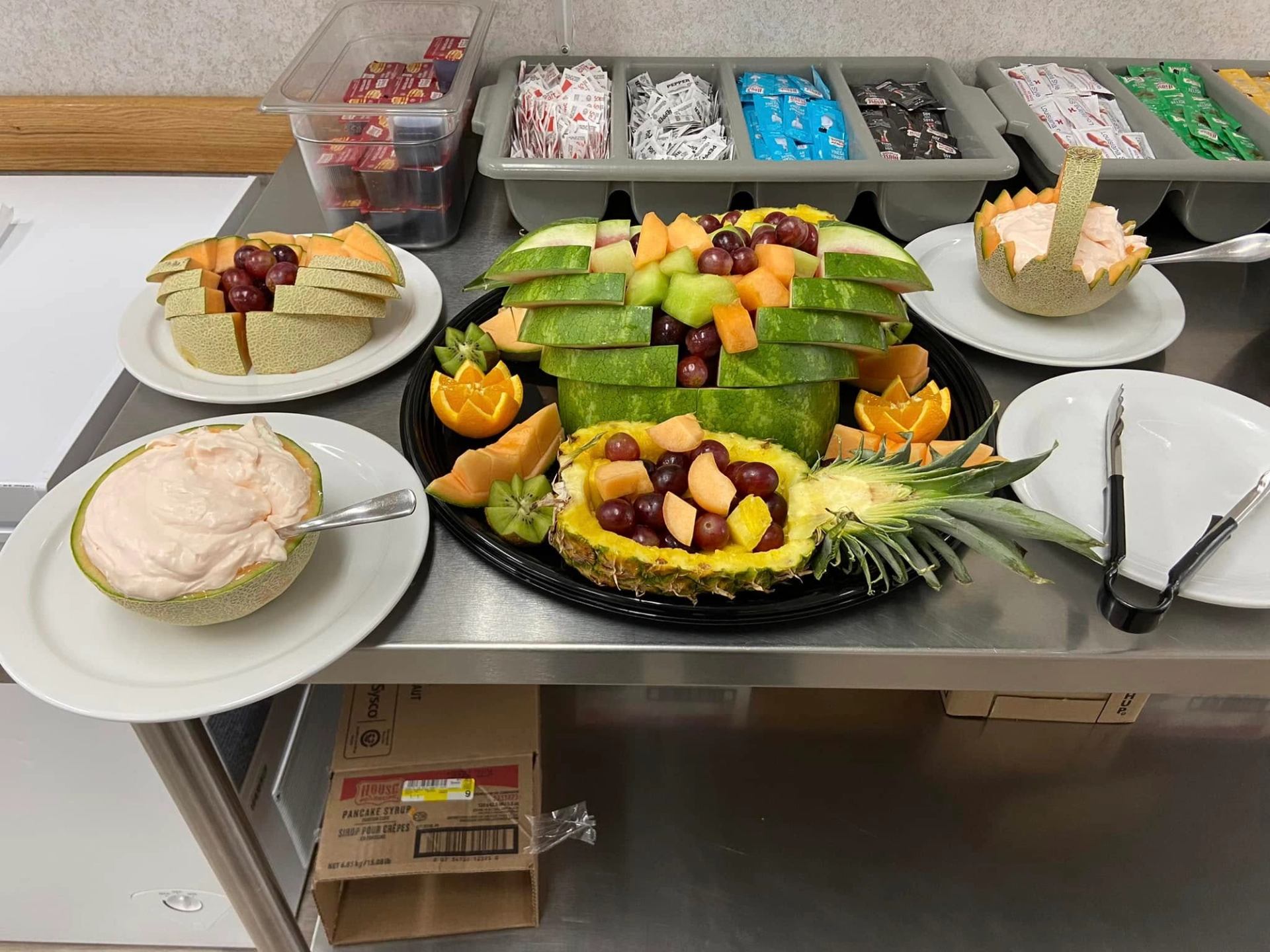 Fruit platter with carved melon bowls, pineapple boat, grapes and dip on buffet counter.