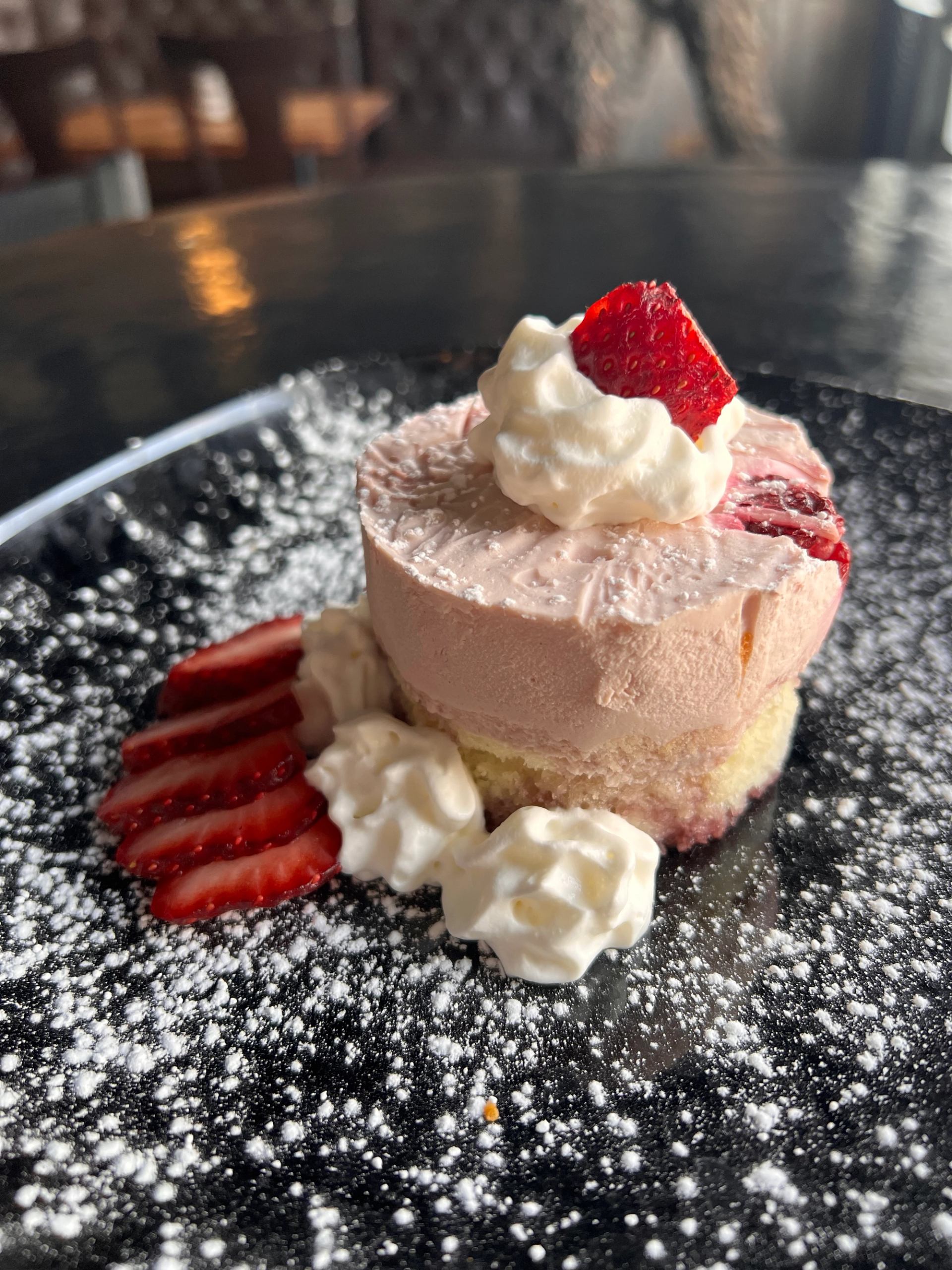Strawberry mousse cake with whipped cream, fresh strawberries, and powdered sugar.