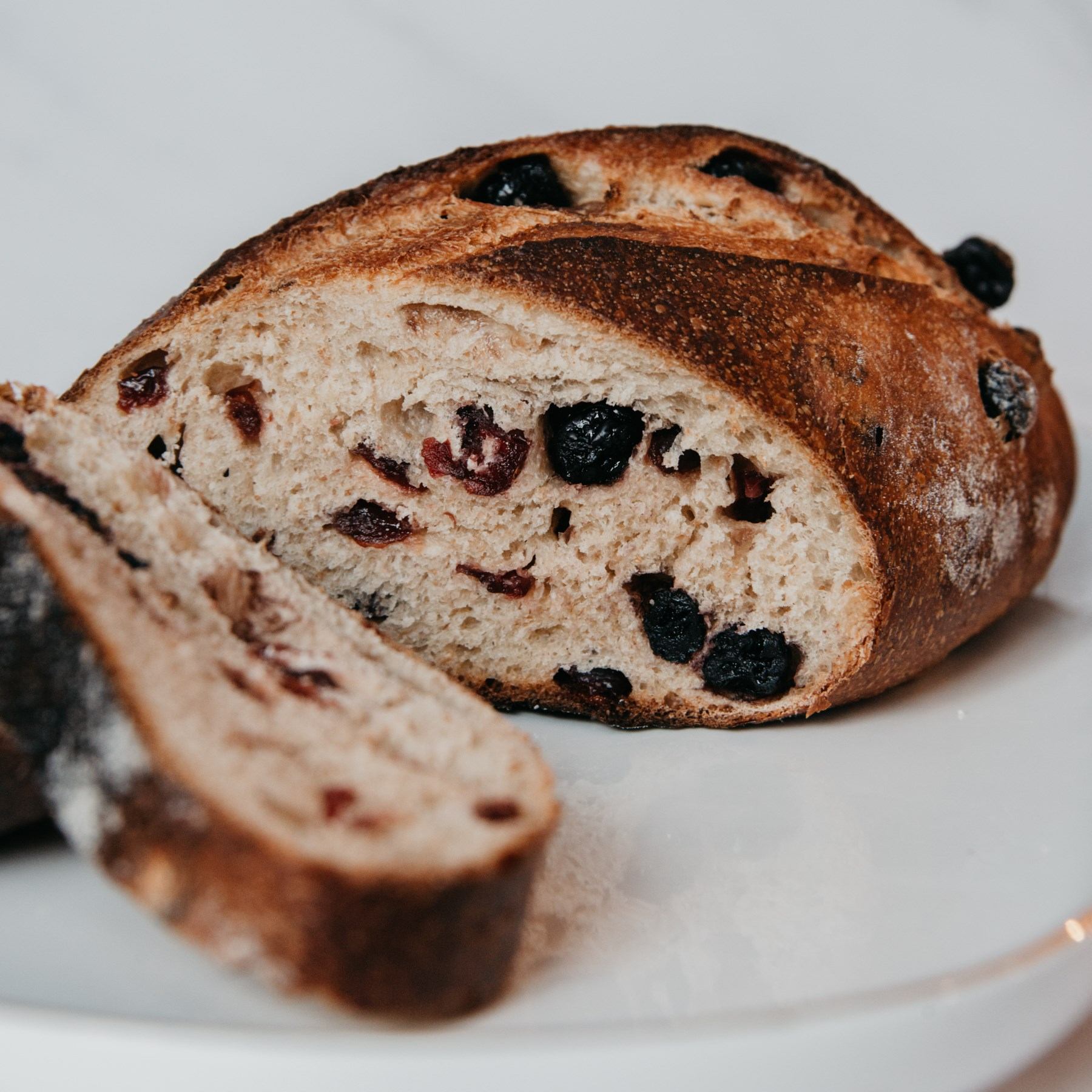 Loaf bread slice with raisins, close-up on crumb and crust texture on white surface.