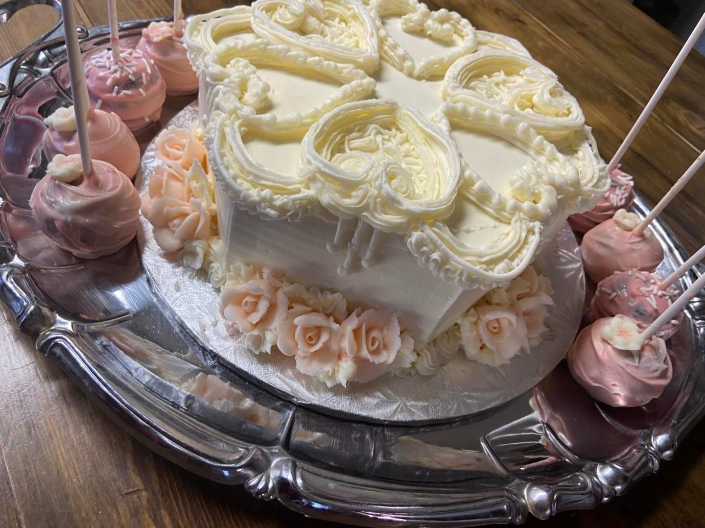 Frosted cake on a silver platter with pink and white mini cupcakes and swirled frosting.