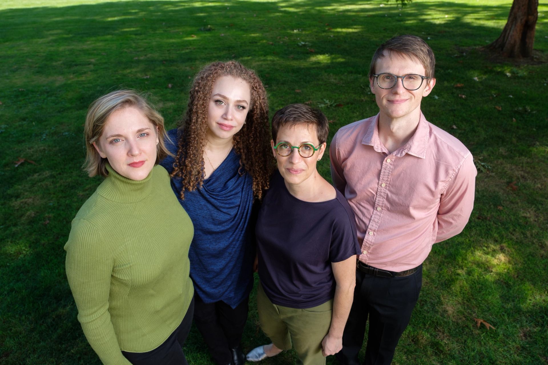 Four people stand closely together on green grass, looking up toward the camera.