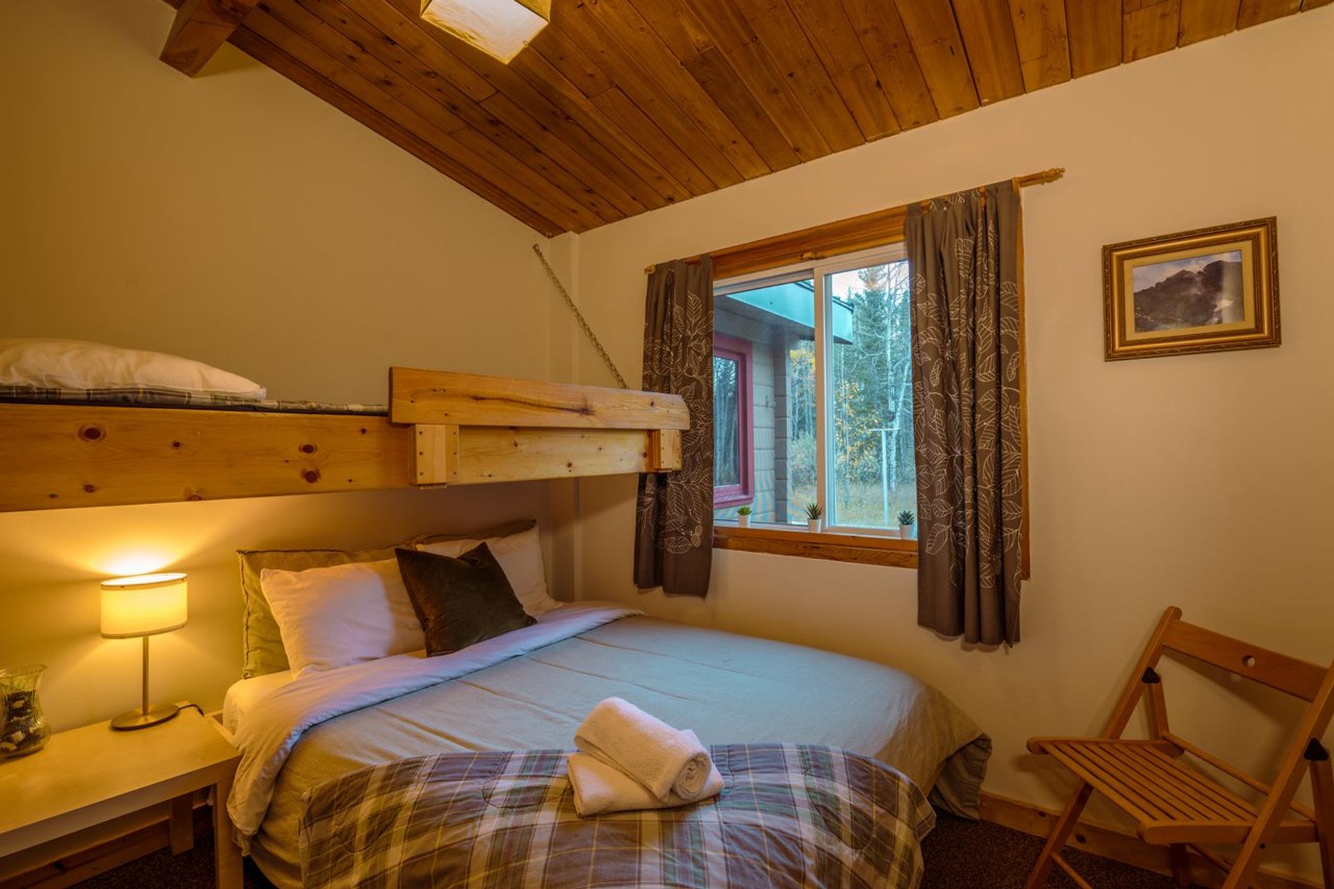 Private room with bunk bed, double bed with plaid bedding, wooden furniture, and vaulted ceiling.