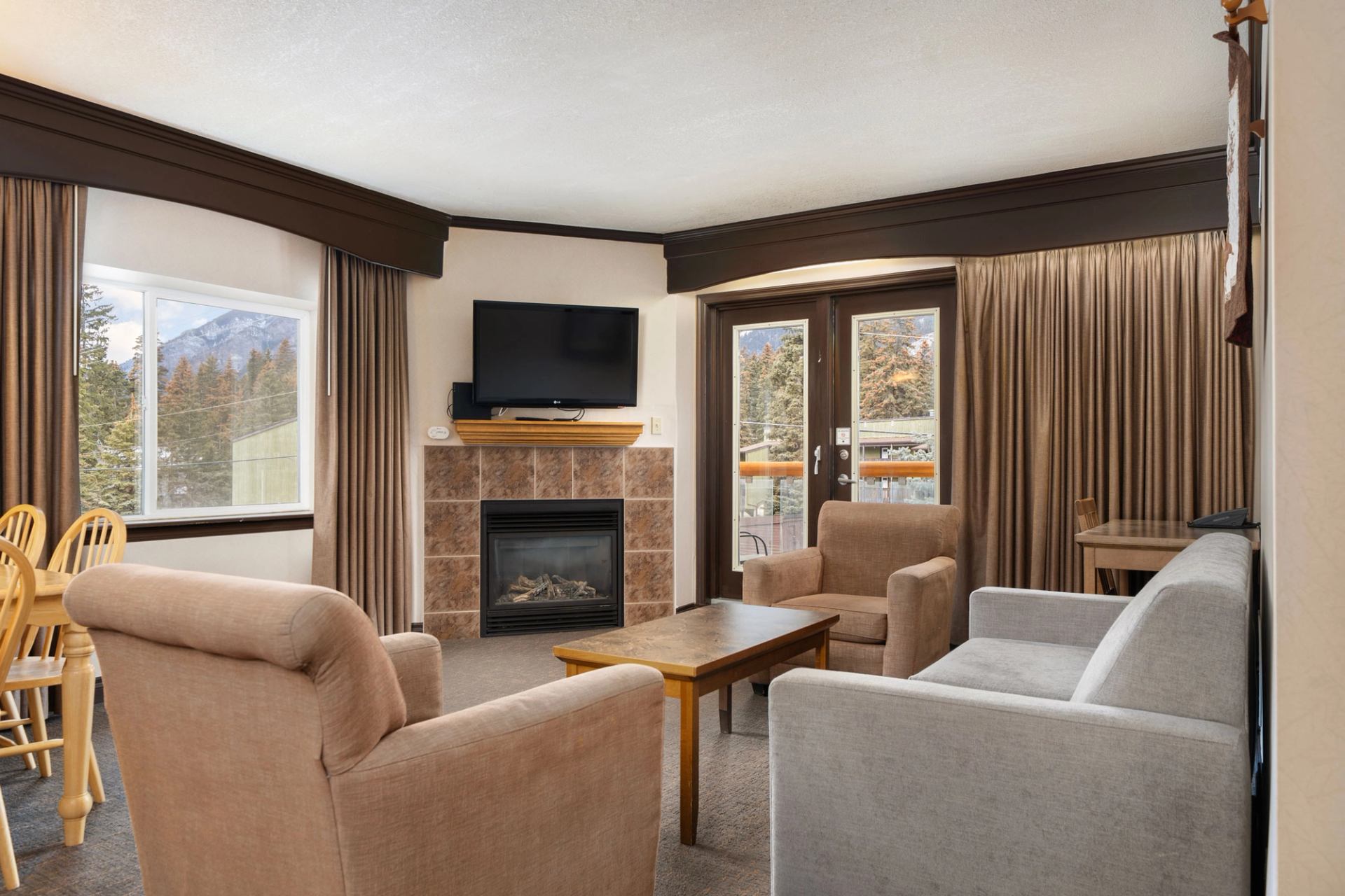Warm lodge living room with fireplace, seating, and large windows.