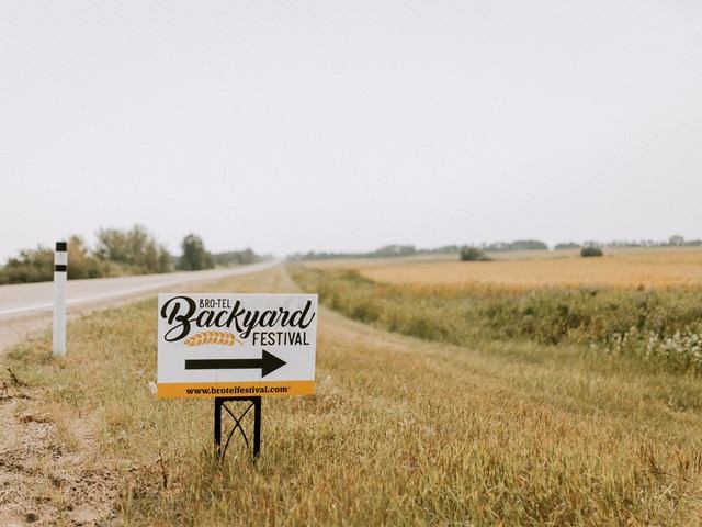 Backyard Festival sign by roadside in a field of grass and crops.