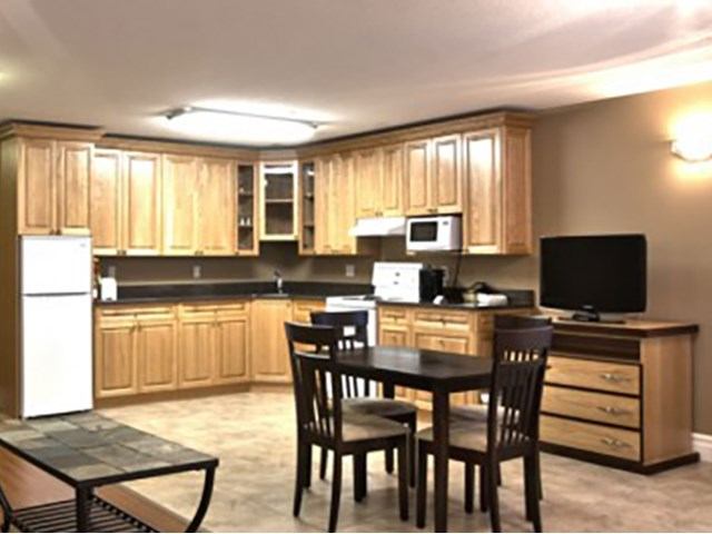 Kitchenette with wooden cabinets, dining table, and TV in a motel suite.