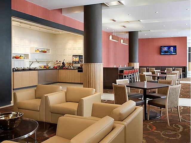 Hotel lounge with beige seating, buffet counter, and red accent wall.