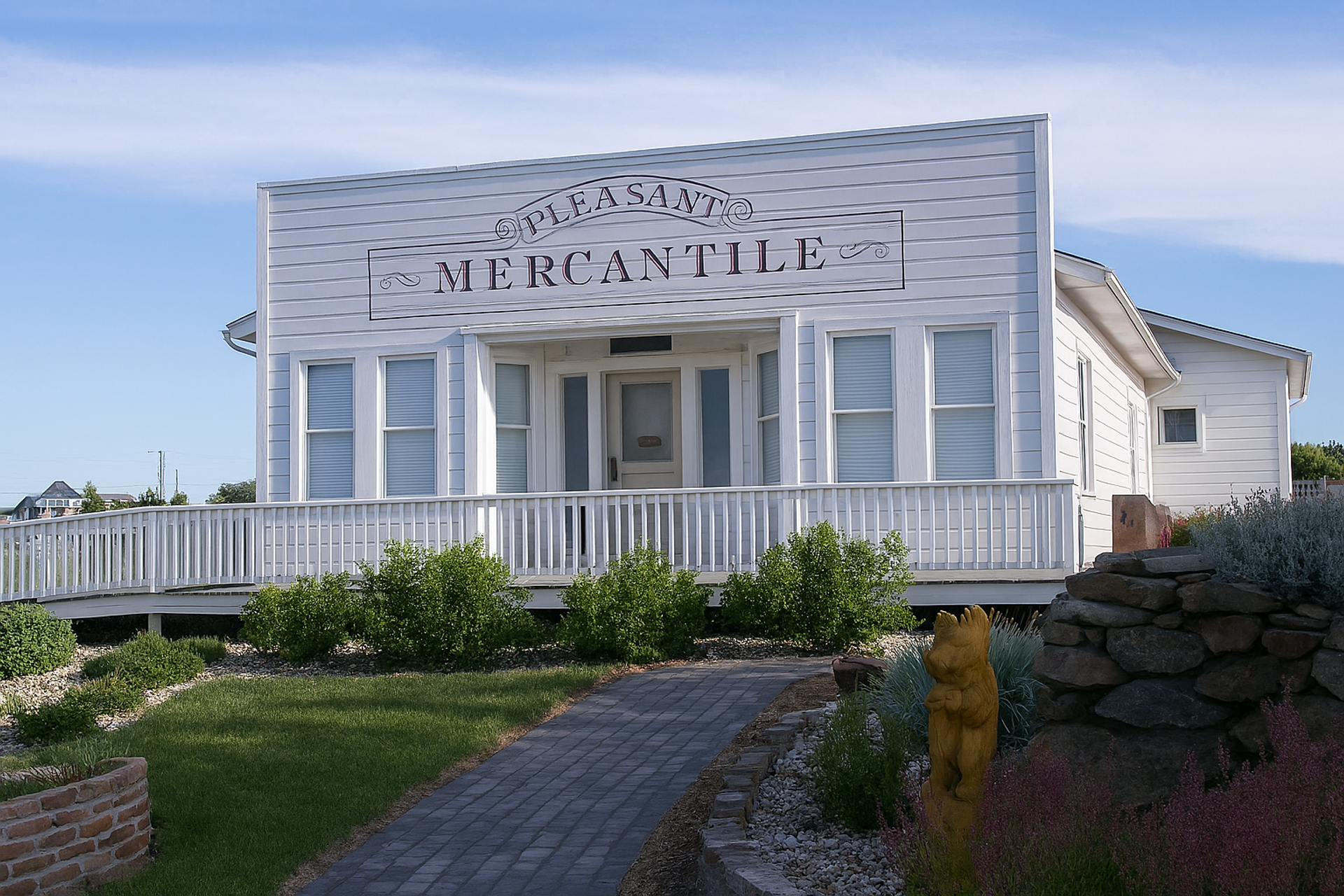 White historic mercantile building with a front porch and walkway leading through a garden.