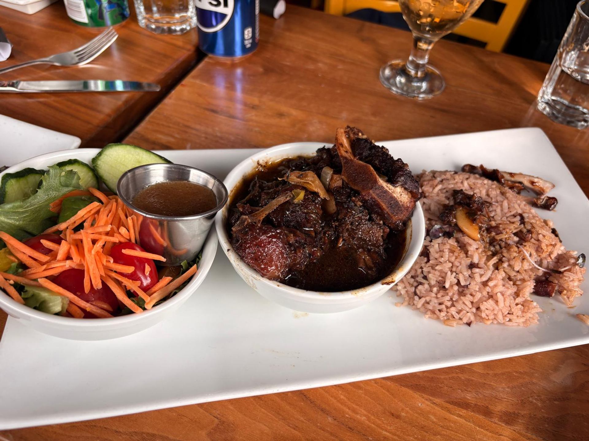 Plate of braised meat, rice and peas, salad and dressing.