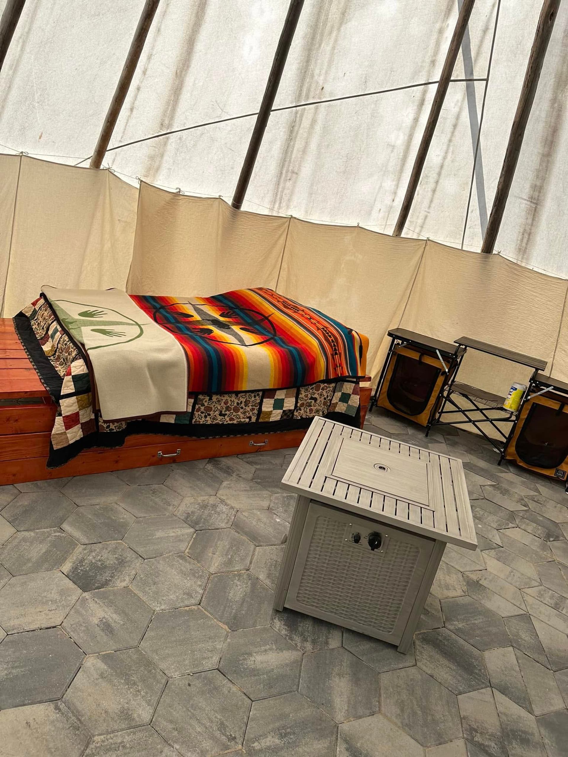 Interior of a tipi with colourful blankets on a wooden bed and small table.