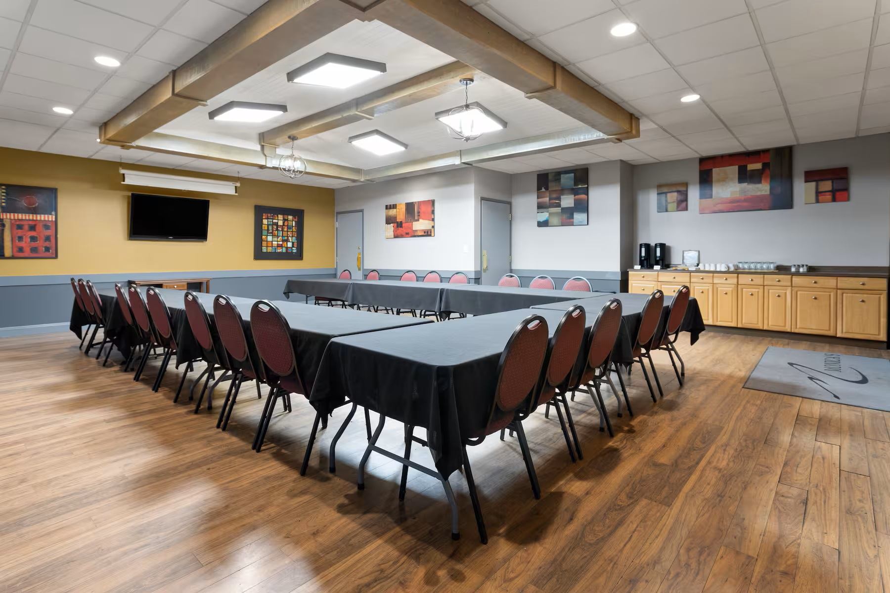 Conference room with U-shaped tables, red chairs, and TV at Travelodge Grande Prairie.
