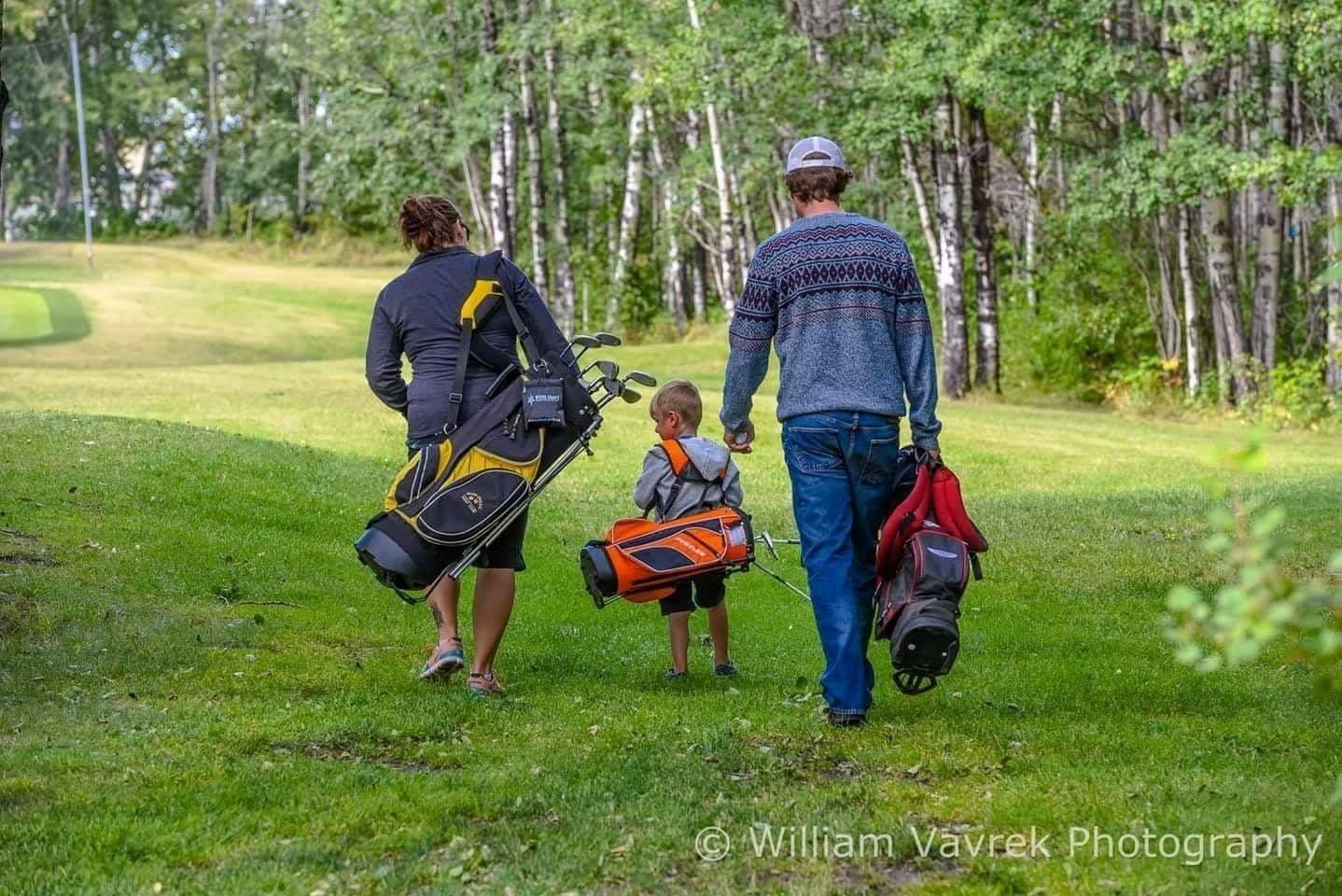 Golfers walking along a fairway with golf bags and clubs through a forested course.