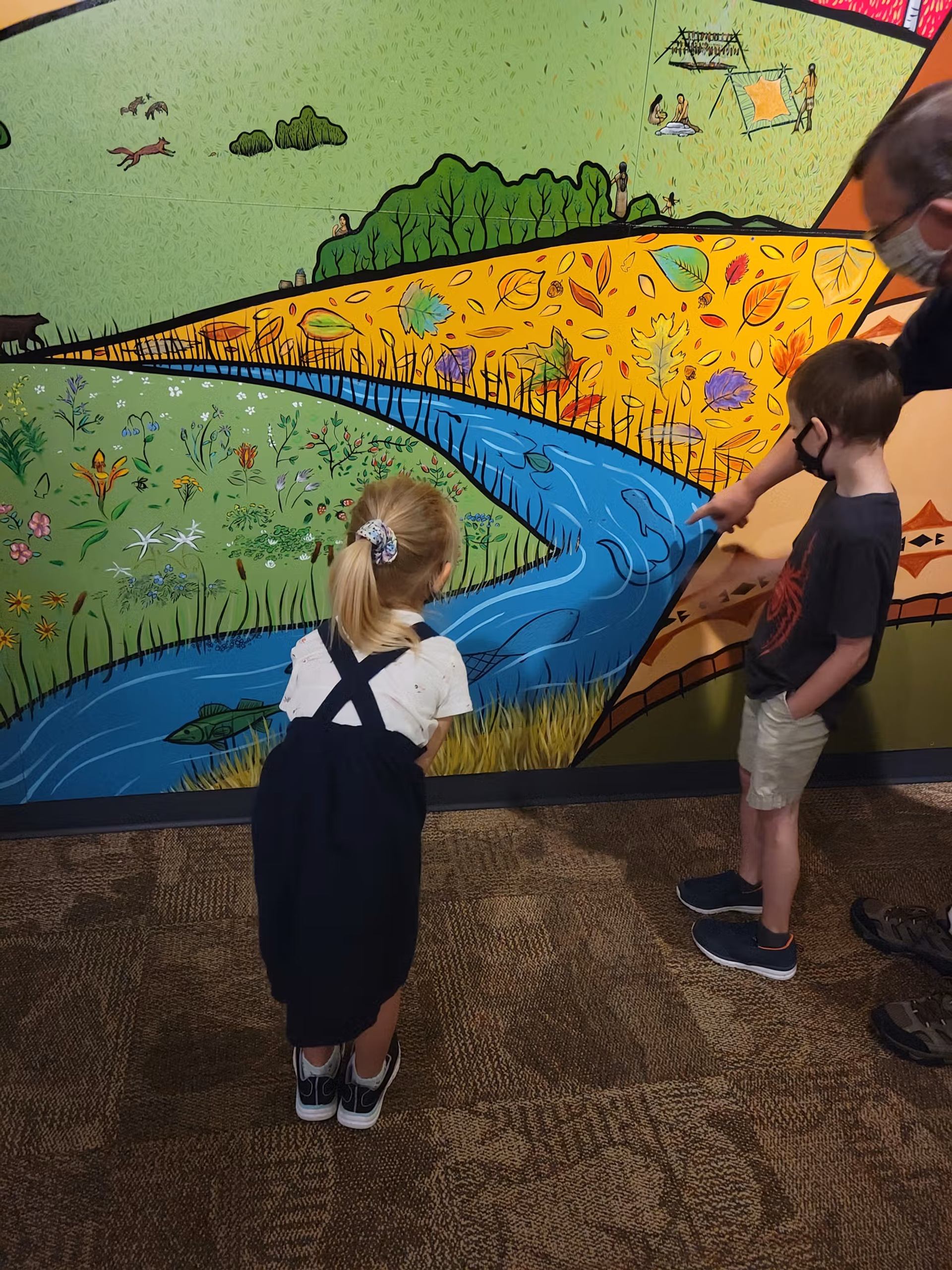 Children stand beside a colourful mural with fish, plants, and a river scene.