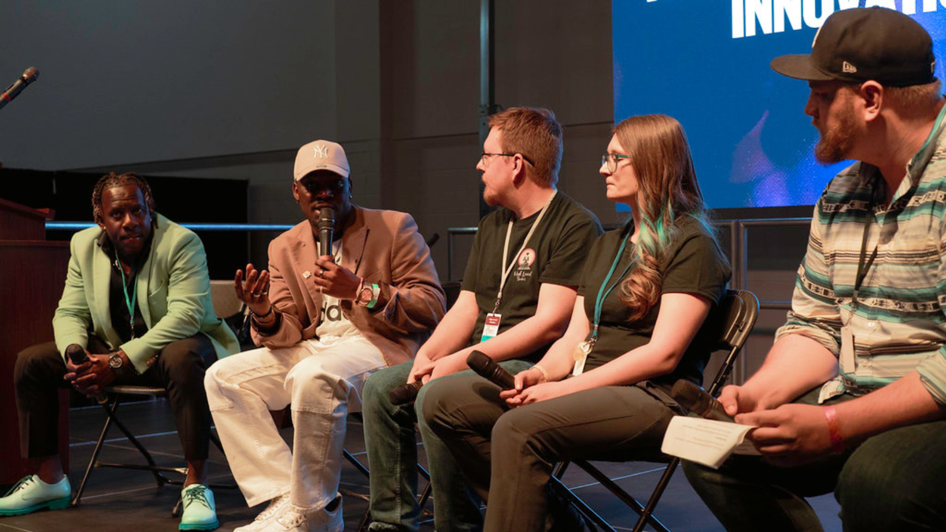 Group of panelists seated on stage speaking into microphones during a conference session.