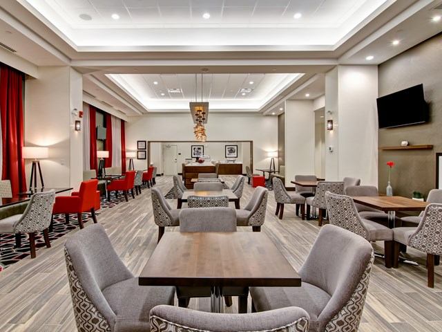 Dining area at Hampton Grande Prairie with tables, red curtains, and wall-mounted TV.