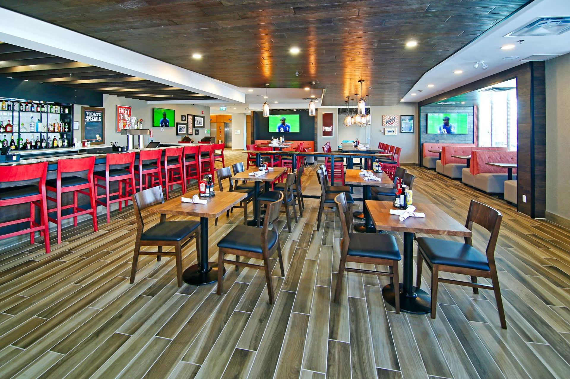 Restaurant with wooden tables, red bar stools, and TVs on the wall