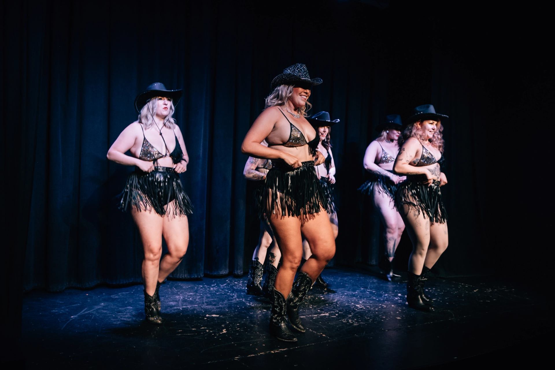 Five performers in cowboy hats and fringed outfits dancing on stage.