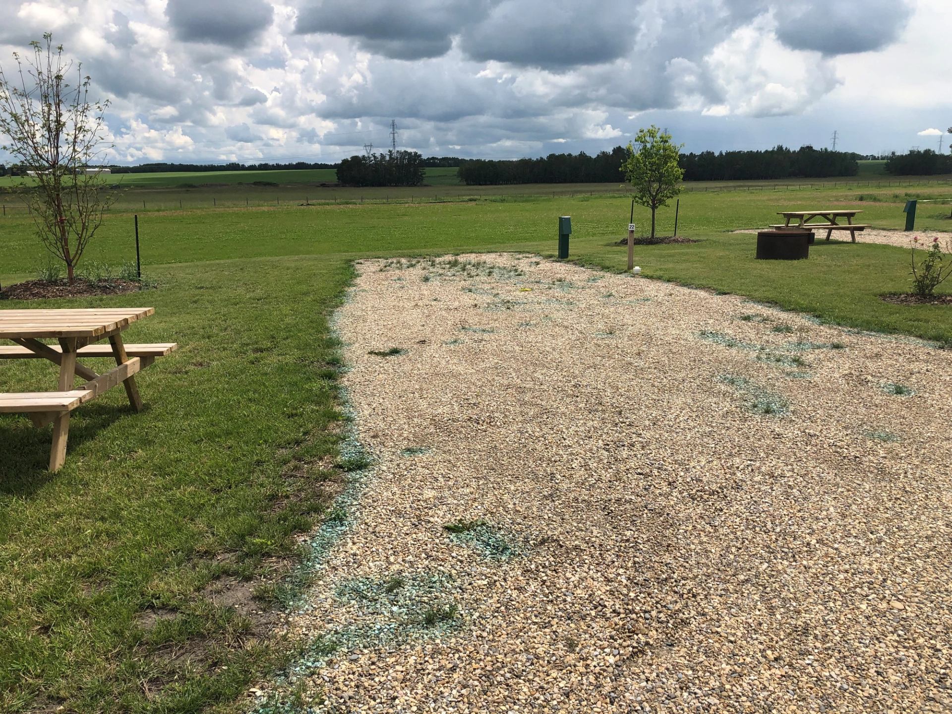 Gravel RV site with picnic table and fire pit on grassy field under cloudy sky.
