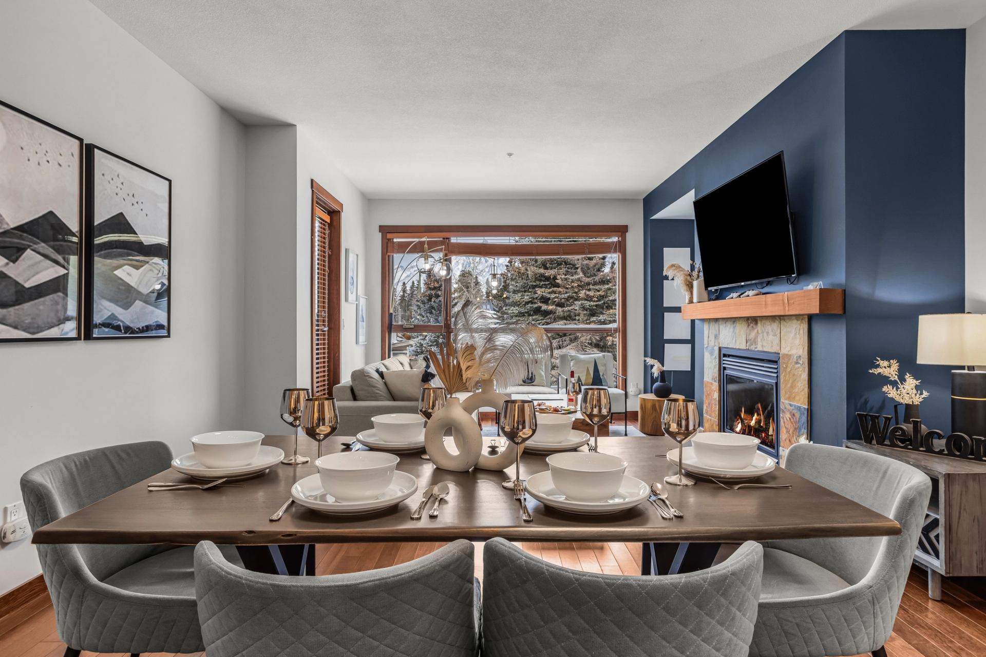 Dining table set with dishes in open living room with fireplace and large window.