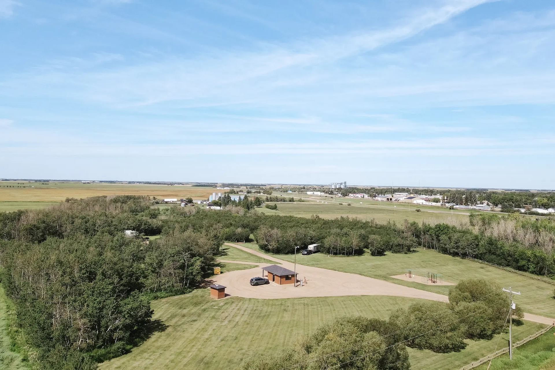 Aerial view of rural park with trees, playground, small buildings and surrounding farmland.