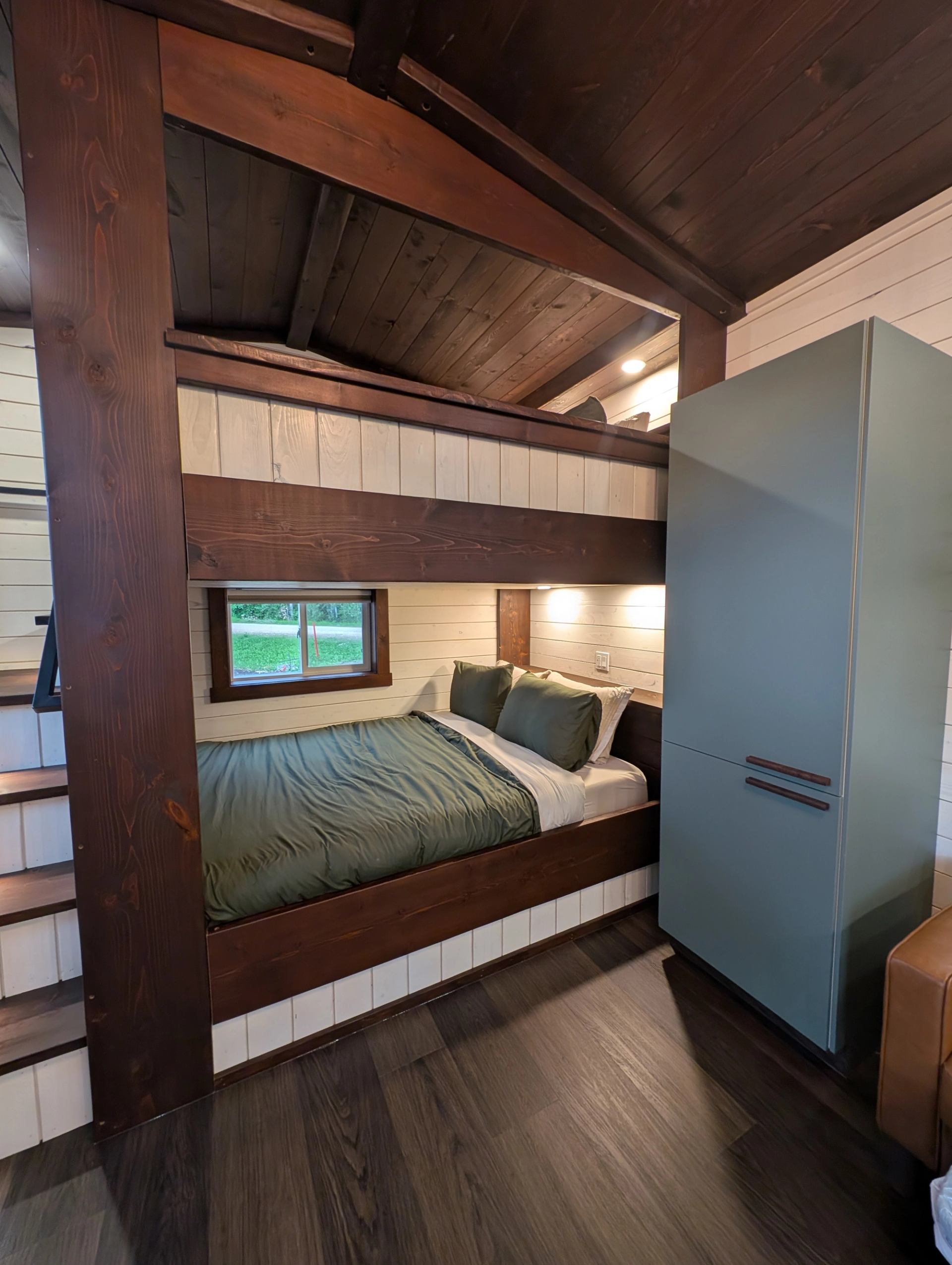 Built-in bed beneath a loft beside stairs and a tall blue cabinet.