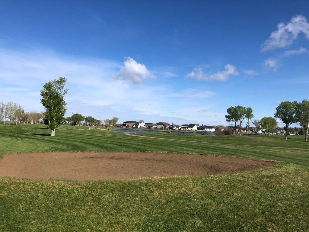 Fairway with a sand patch and houses in the distance under a clear blue sky.