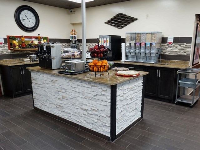 Hotel breakfast area with island, coffee machines, and cereal dispensers.