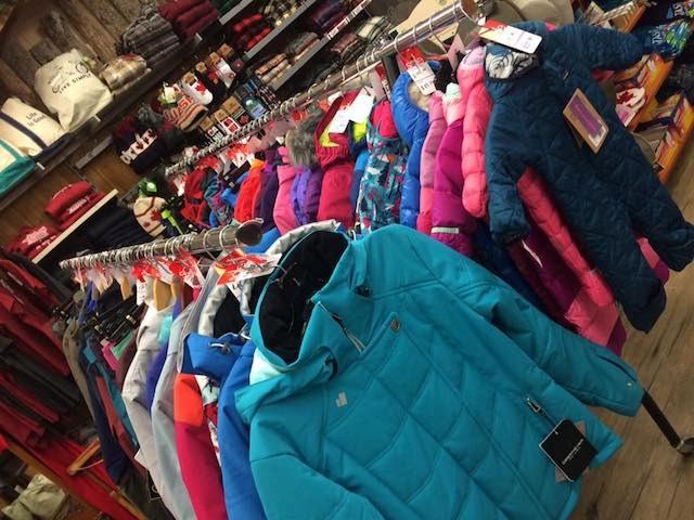 Colorful winter jackets and snowsuits hanging on racks in a ski shop display.