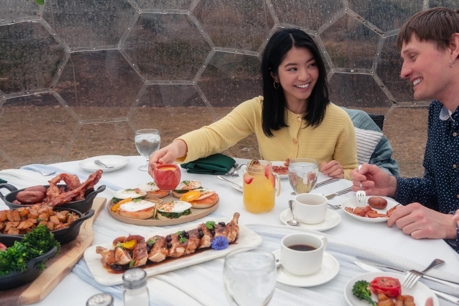Guests sit at a table inside a garden dome enjoying brunch dishes and drinks.