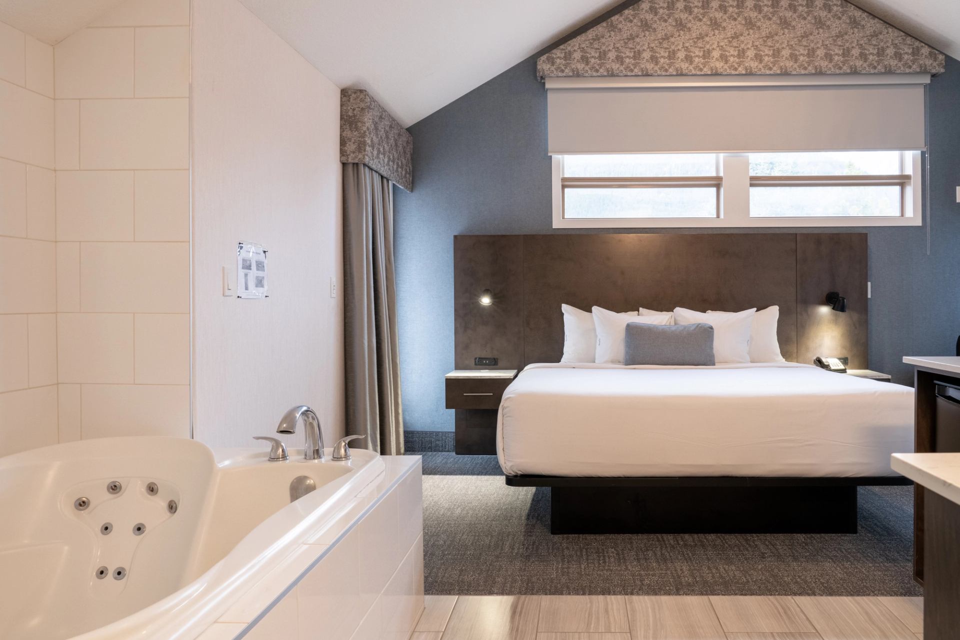 Modern hotel room with bed, windows, and in-room jacuzzi tub.