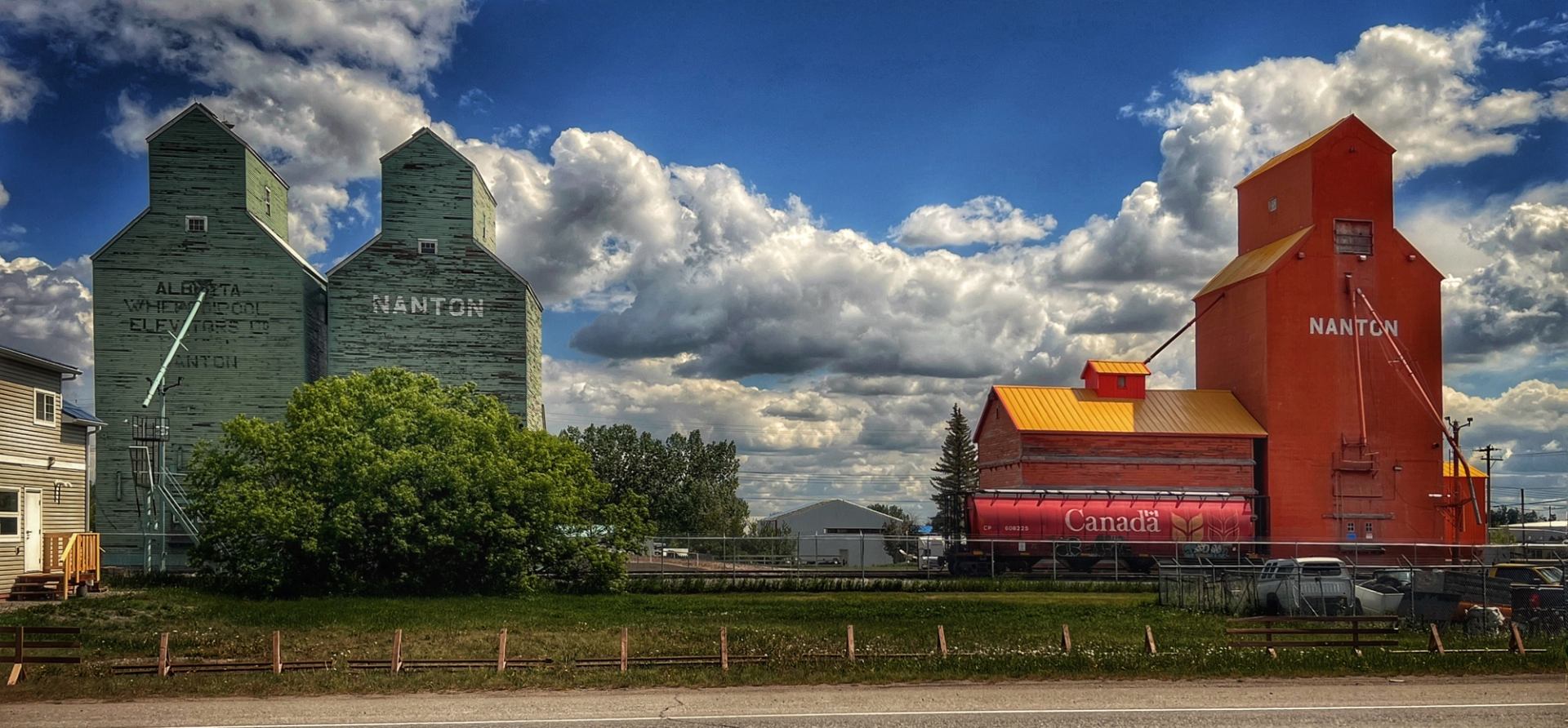Row of green and red grain elevators under a wide blue sky.