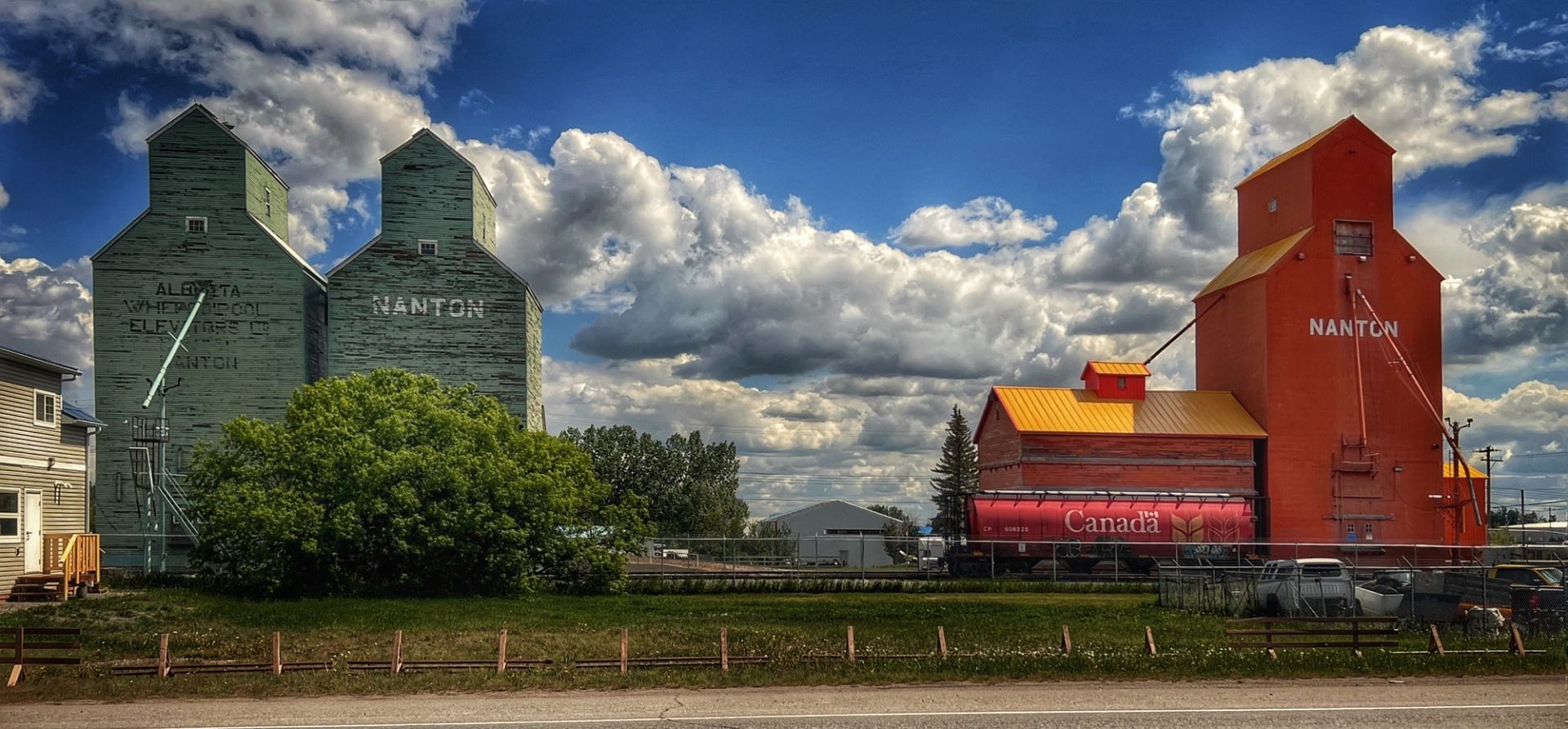 Row of green and red grain elevators under a wide blue sky.