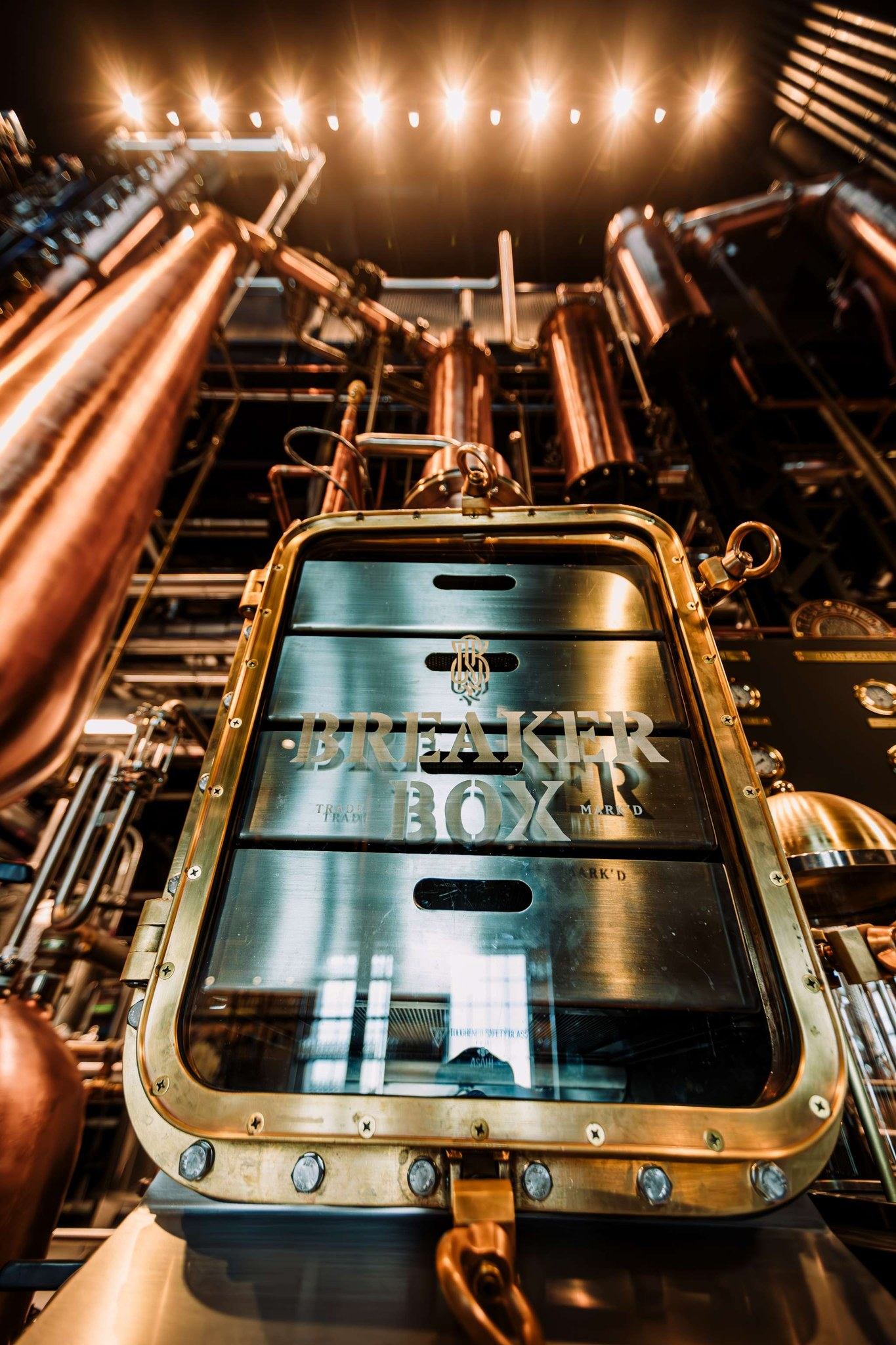 Close-up of copper distilling equipment and pipes with a “Breaker Box” panel inside True Wild Distillery.