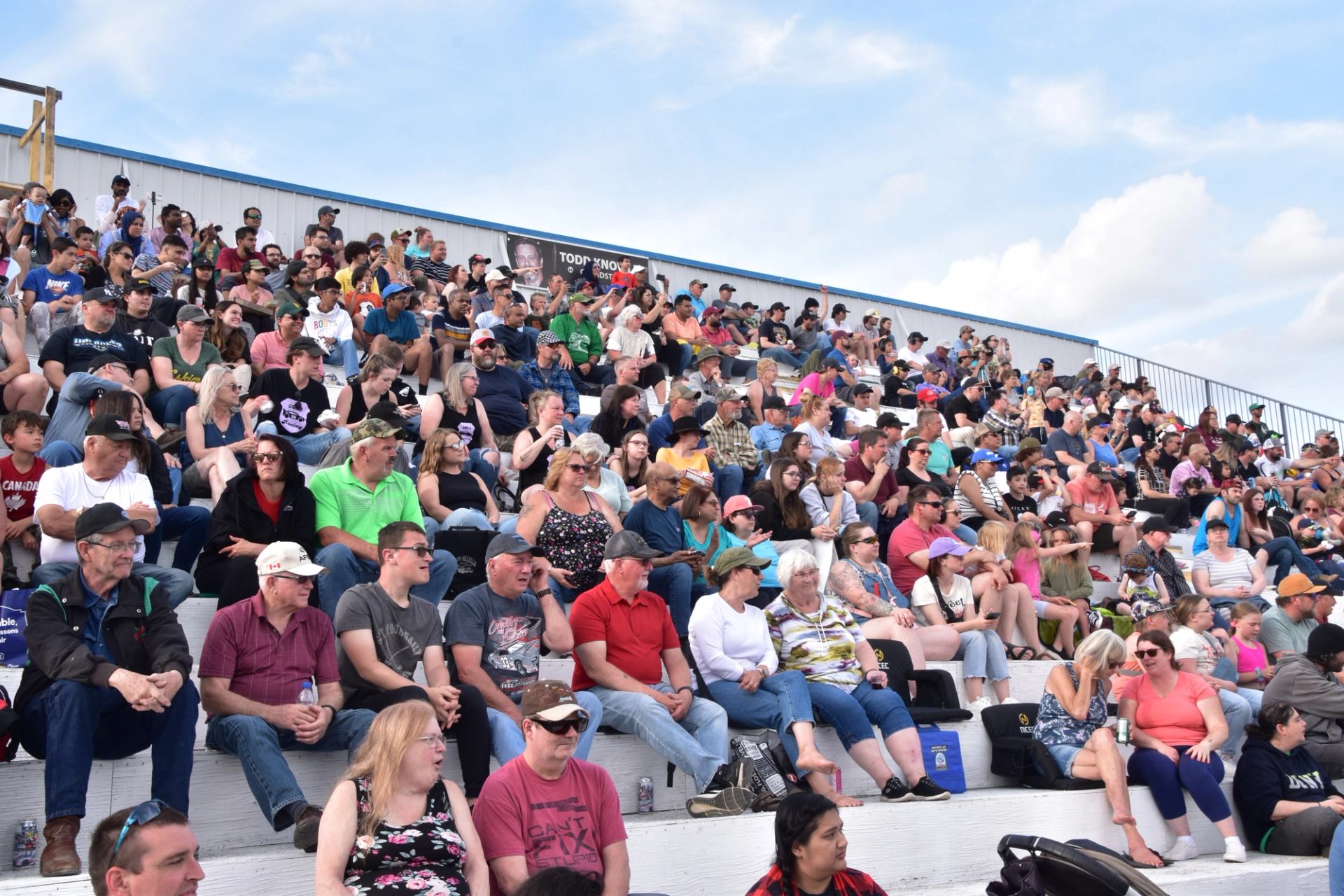 Grandstands filled with fans at the NASCAR Canada NAPA 300 under a bright blue sky.