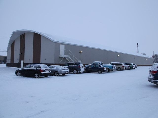 Snowy scene with a curved-roof building and parked cars in front.