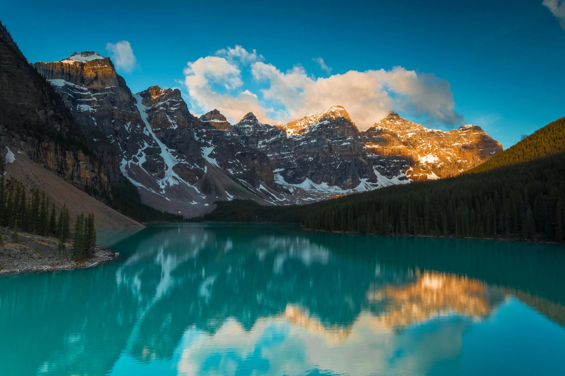 Snow-dusted mountain peaks and evergreen forest reflect in a turquoise lake.