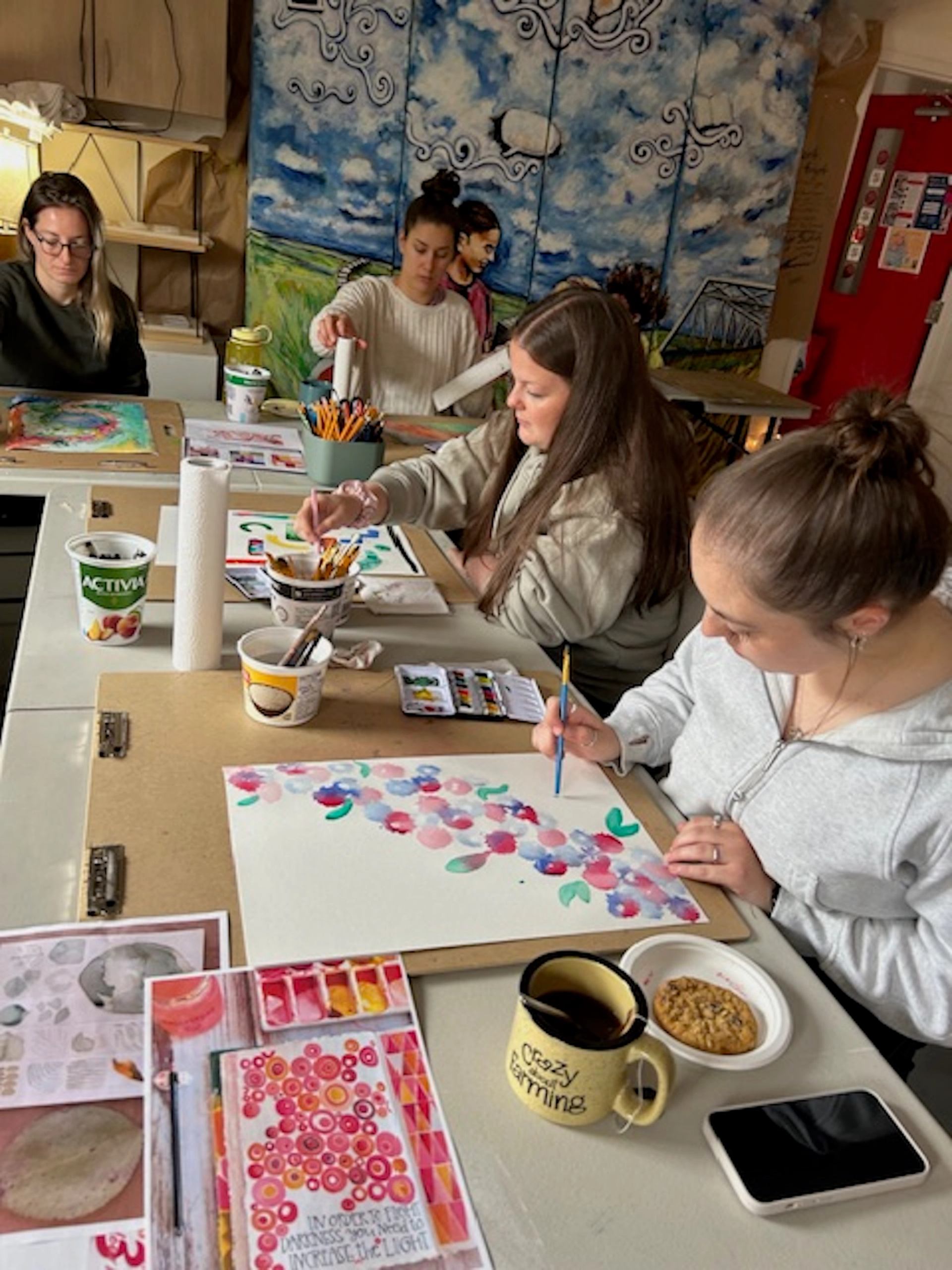 People seated at a table painting colourful artwork with supplies and snacks.