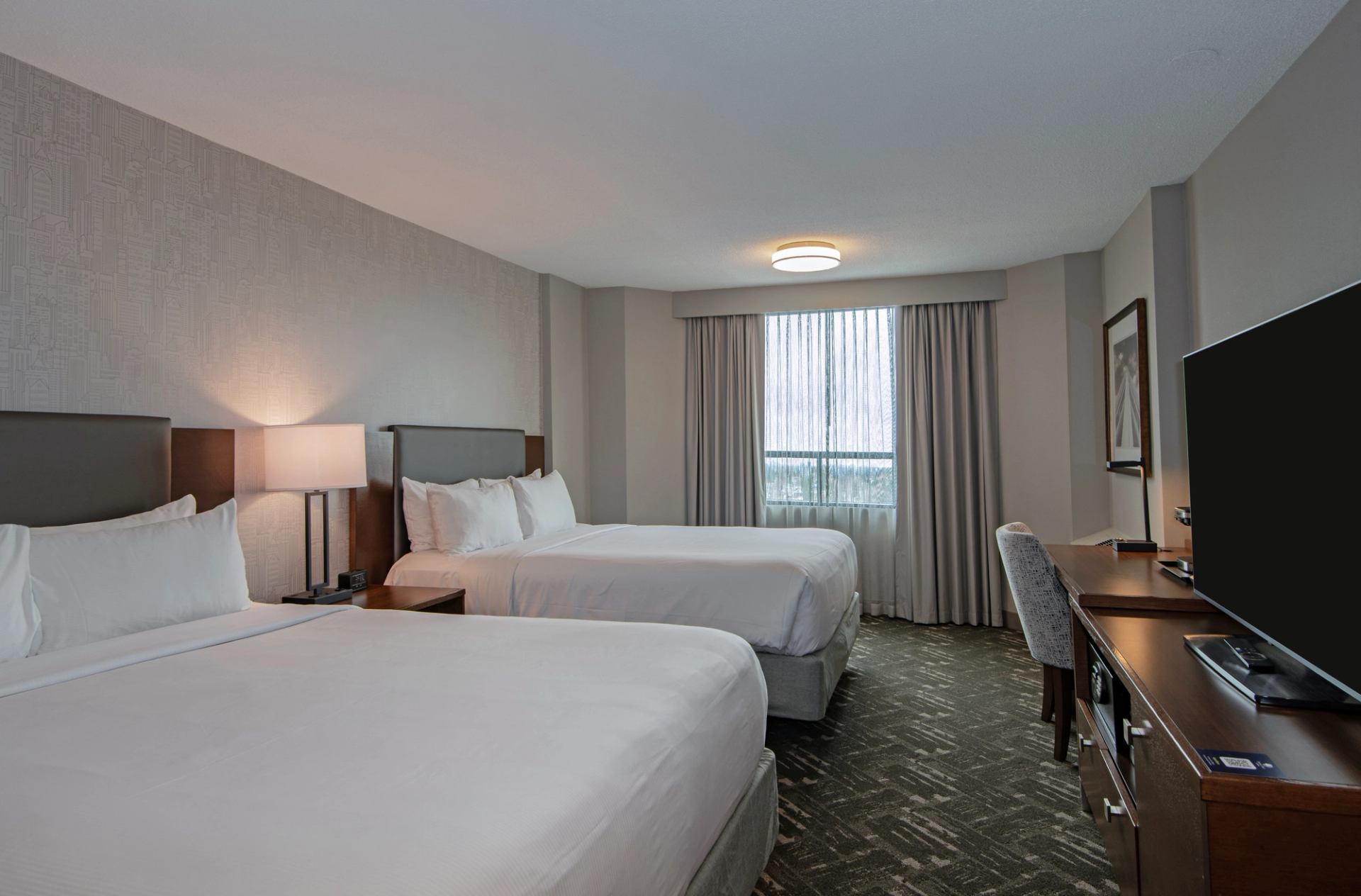 Hotel room with two double beds, window with curtains, desk, chair and television.