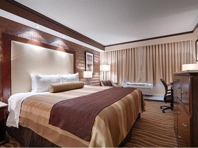 Warm hotel room with large bed, desk, armchair, and soft lighting.