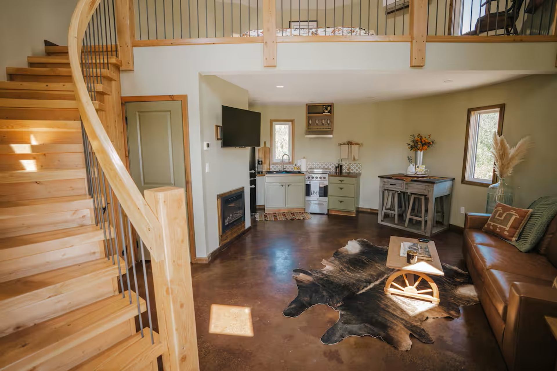 Rustic Saddle Hill Ranch cabin interior with wood staircase, leather sofa, and kitchenette.
