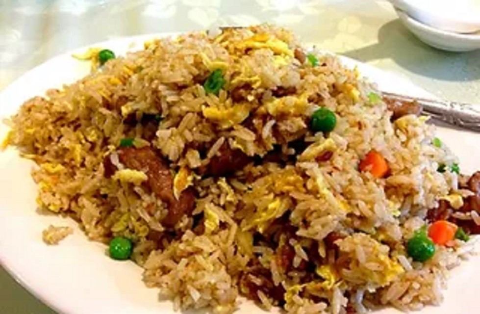 Fried rice with vegetables, egg, and tender meat served on a white plate.