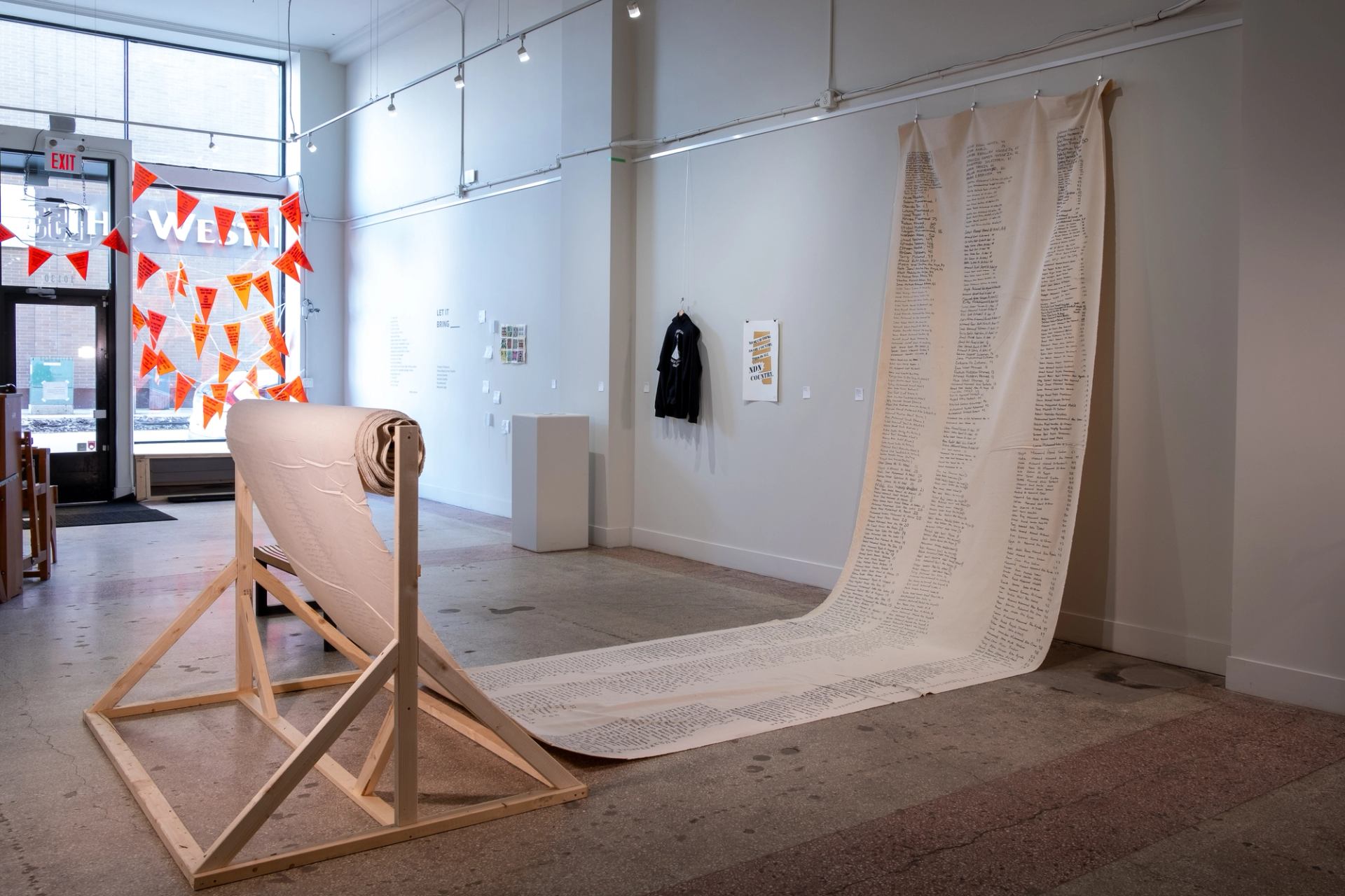 Large scroll hangs from white gallery wall, with small black text written across the canvas.