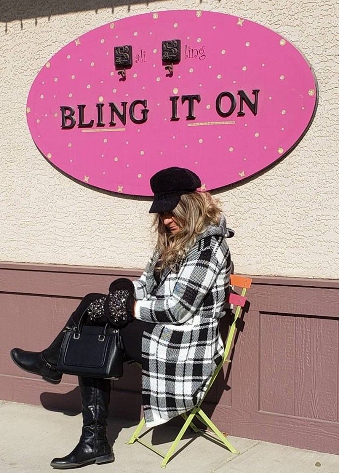 Person sits on folding chair under pink Bali Bling sign reading “BLING IT ON”.