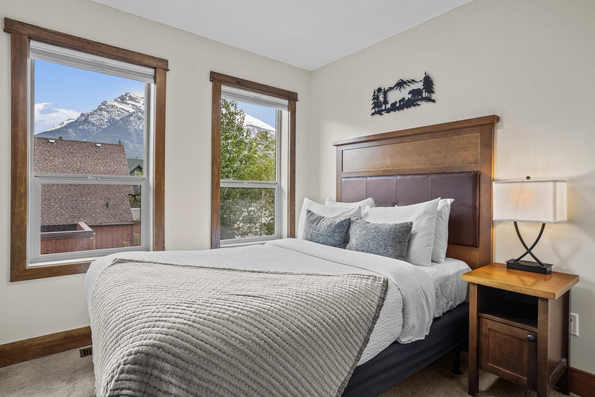 Bedroom with wooden bed, bedside lamp and windows overlooking snow-capped mountains.
