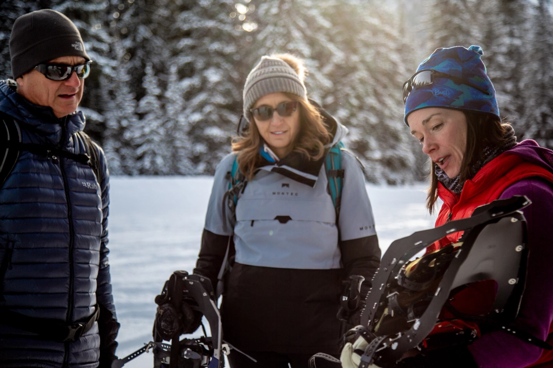 Close-up of snowshoes held by a person wearing winter gear in a snowy forest setting