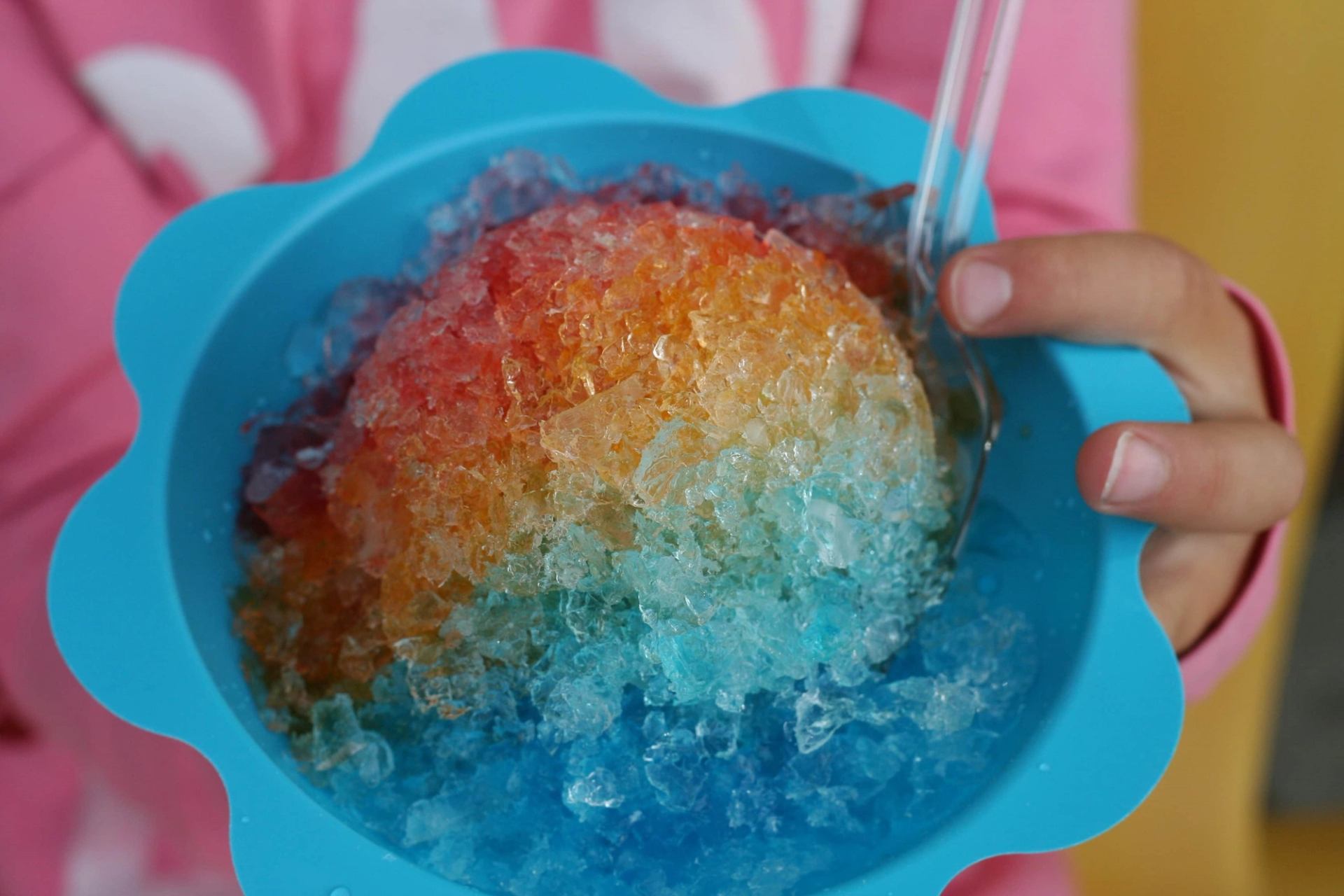 Colorful shaved ice in a blue flower-shaped bowl with a straw.